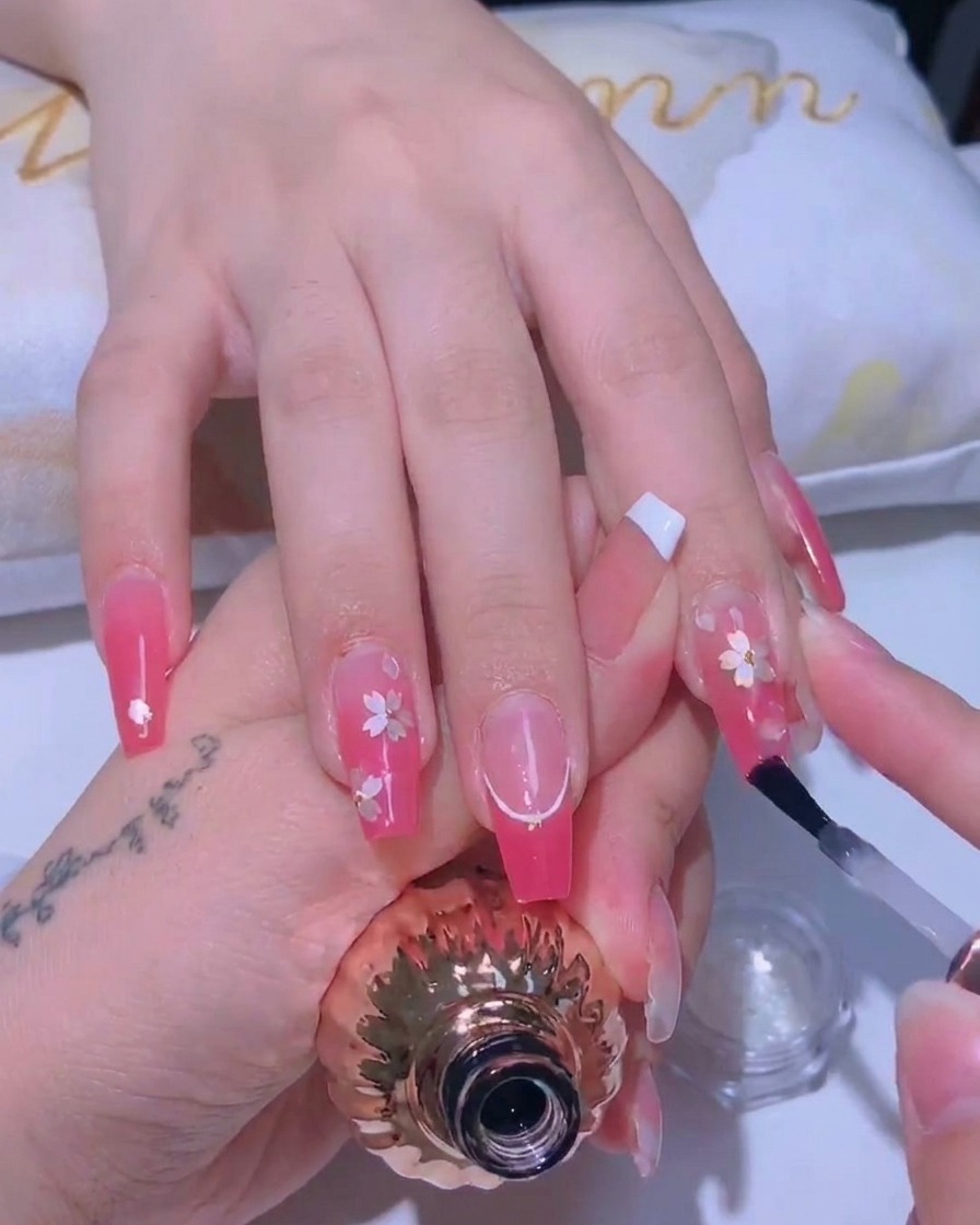 Un pinceau à ongles appliquant une fine couche de top coat brillant sur un design fleurs de cerisier.