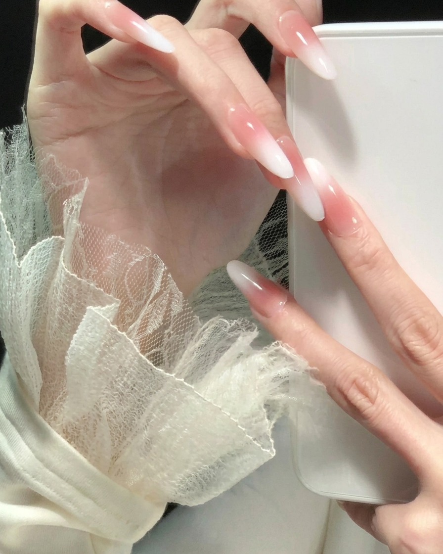 Main aux doigts écartés, mettant en valeur un dégradé rose vers blanc cohérent sur tous les ongles longs en forme damande.