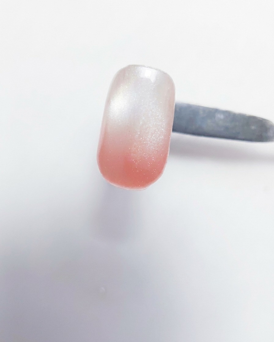 Vue en gros plan dun pinceau gel déposant du gel rose pêche sur le bord libre dun ongle ayant déjà une base blanche laiteuse.