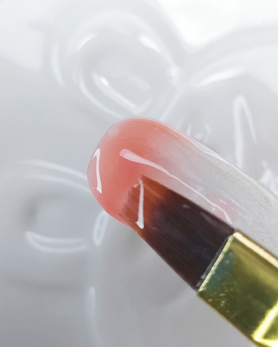 Gros plan dun pinceau étirant le gel rose pêche vers le haut sur une base blanche laiteuse pour créer un effet ombré.