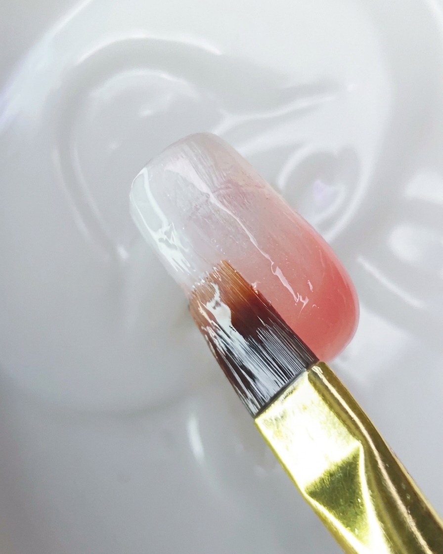 Un pinceau appliquant un top coat transparent sur la surface de longle dégradé.