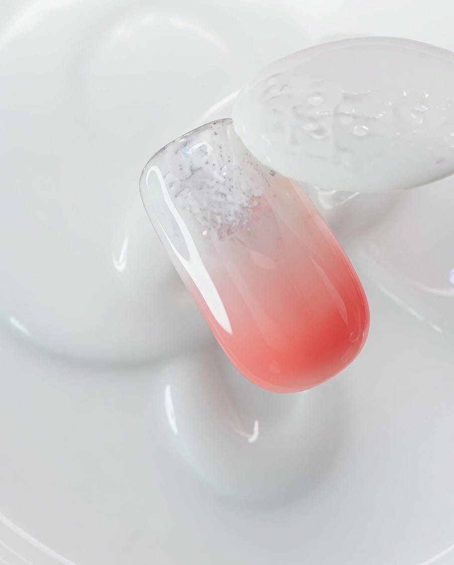 Un pinceau appliquant un gel magnétique transparent sur un ongle recouvert de poudre aurora.