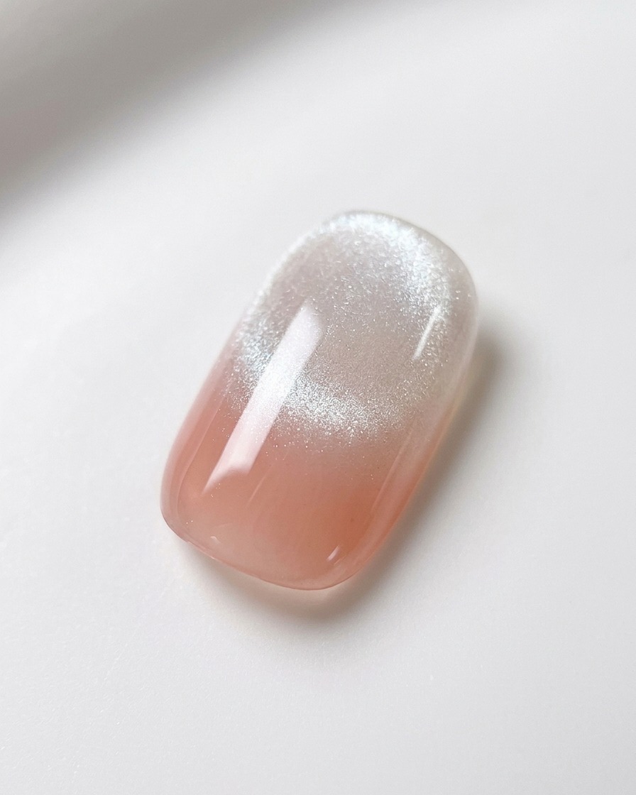 Un aimant à ongle sphérique maintenu au-dessus dun ongle dégradé rose et blanc avec du gel magnétique humide, soulignant la formation dune traînée cat-eye brillante.