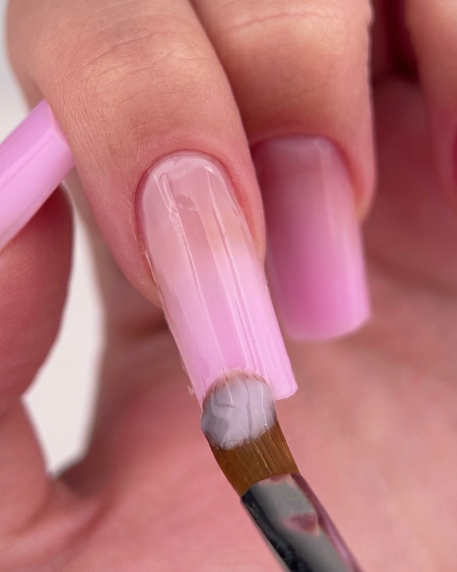 Pinceau appliquant un vernis rose laiteux près de la cuticule.
