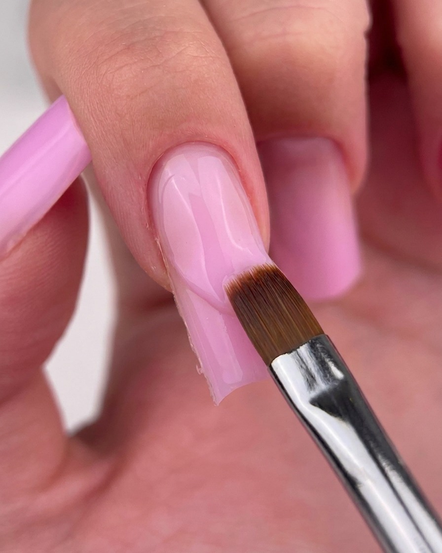 Pinceau fin de précision nettoyant le bord du vernis rose près de la cuticule.