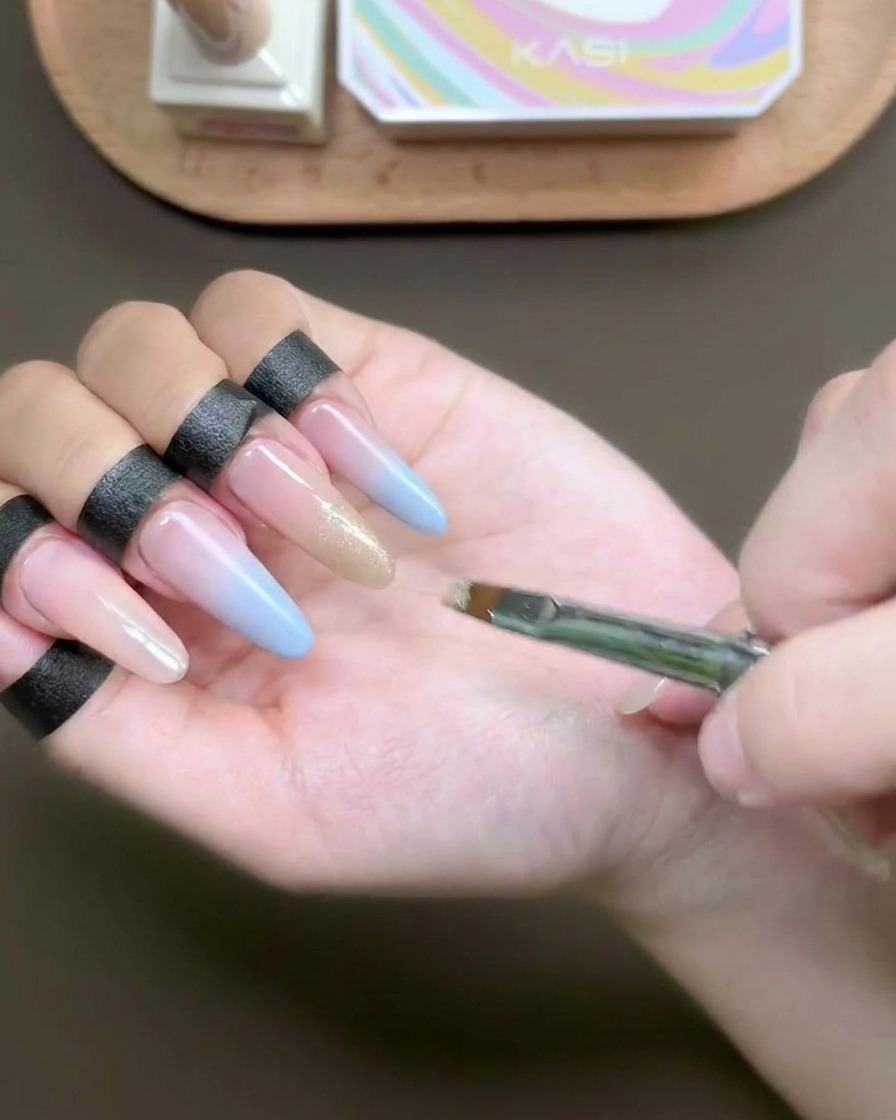 Un pinceau plat appliquant un gel œil-de-chat scintillant champagne sur le bout dun ongle.