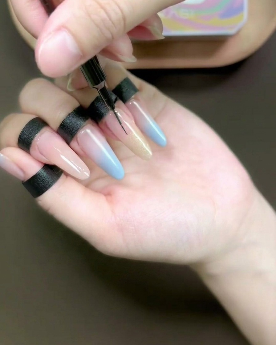 Vue rapprochée dun pinceau liner estompant du gel œil-de-chat couleur champagne sur un ongle long.
