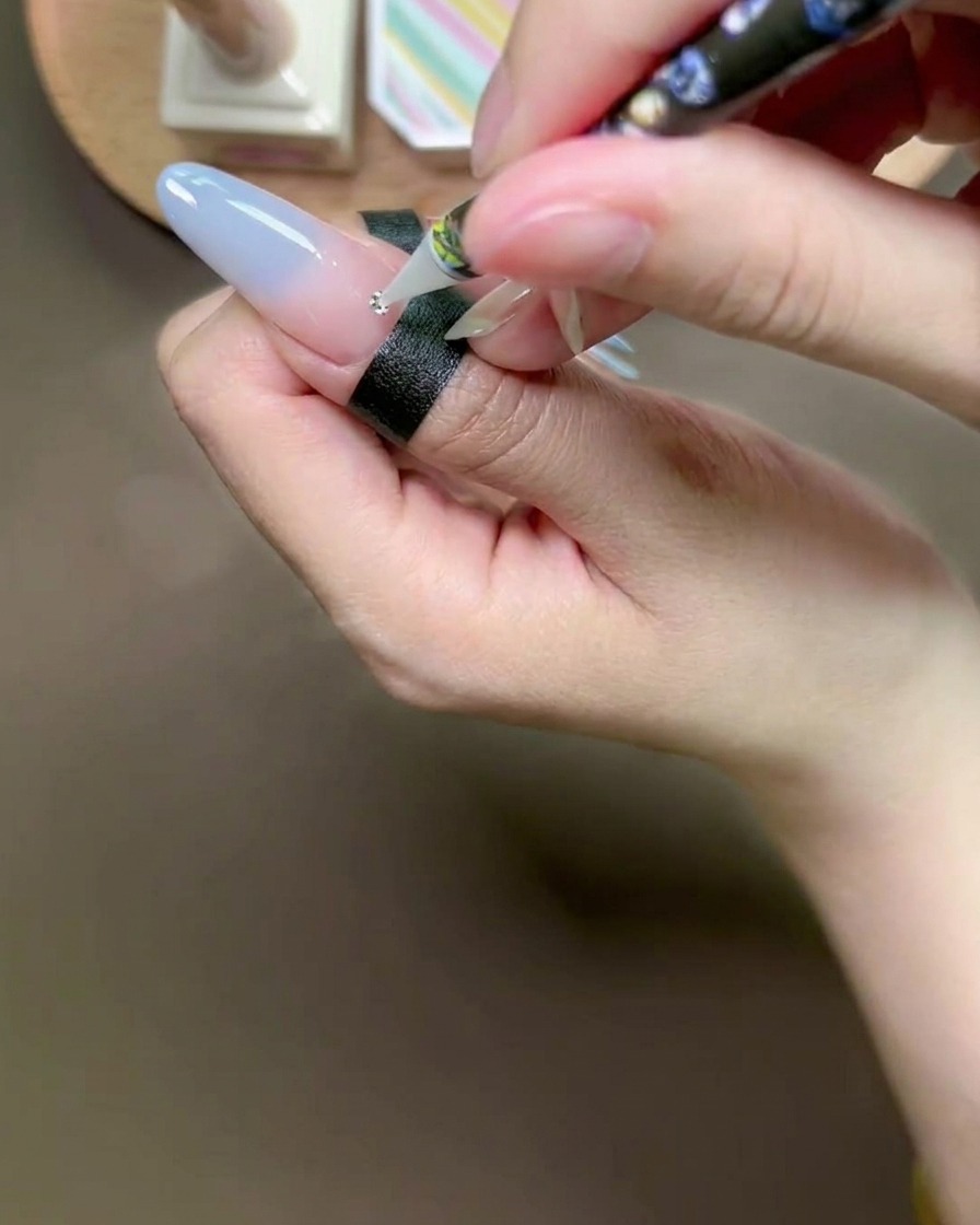 Un stylo applicateur en cire déposant un petit strass argenté sur un point de colle.