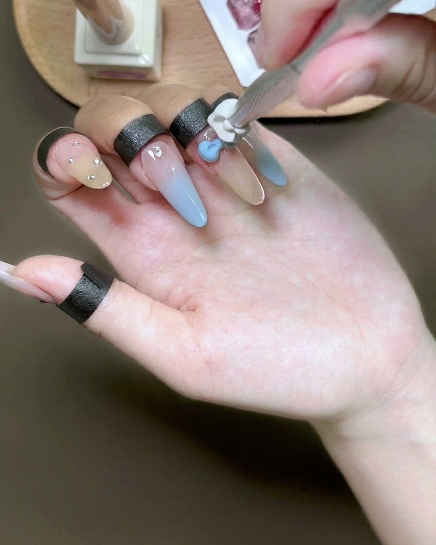 Une éponge tamponnant du gel bleu clair sur un nœud 3D blanc sur un ongle.