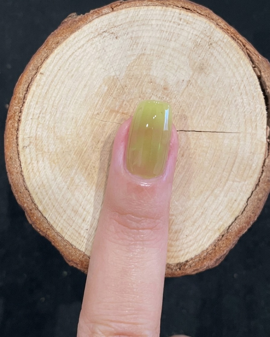 Gros plan dun pinceau appliquant du gel vert translucide sur un ongle naturel.