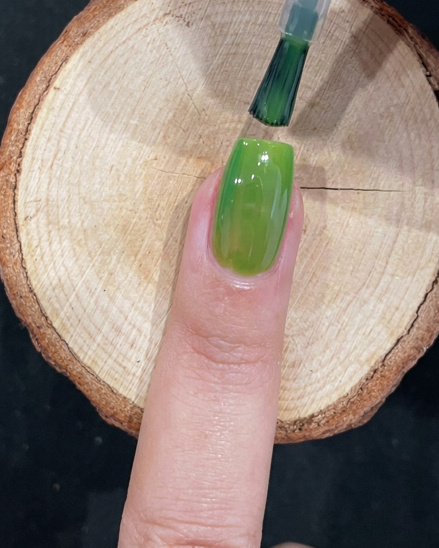 Un pinceau appliquant méticuleusement du gel vert près de la cuticule dun ongle.