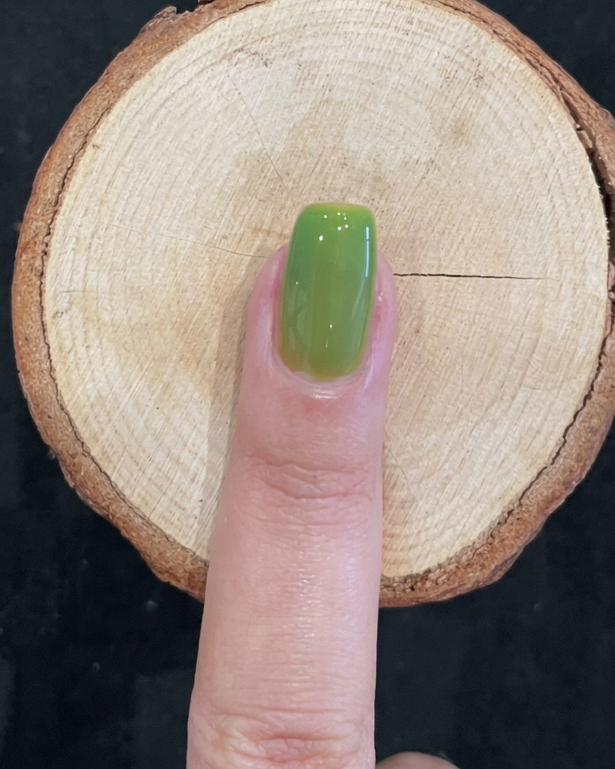 Un ongle propre, brillant et vert translucide catalysé sur une surface en bois.