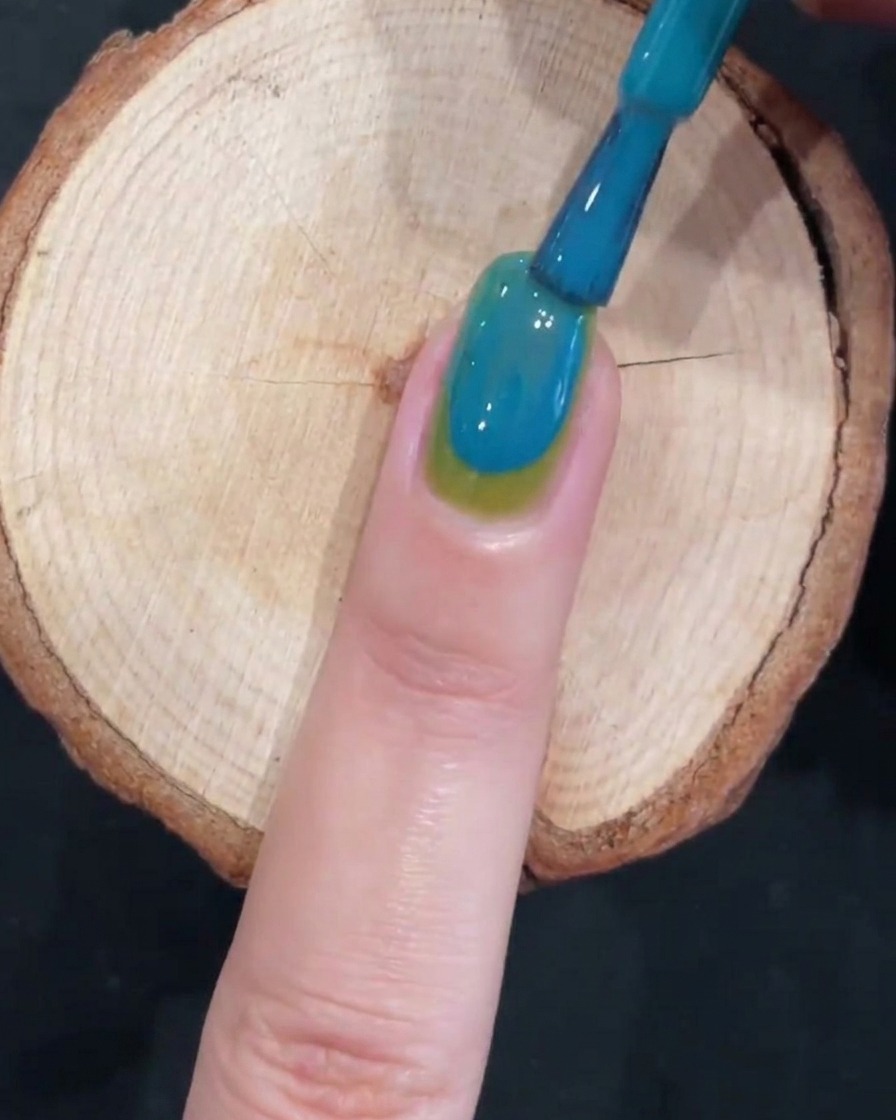 Un pinceau créant un effet dégradé lisse sur un ongle bicolore vert et bleu.