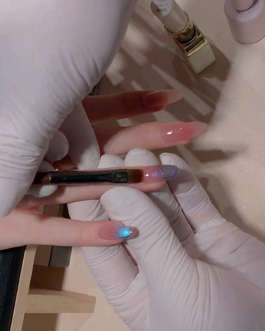 Gros plan sur un pinceau plat estompant le gel cat-eye bleu sur longle.