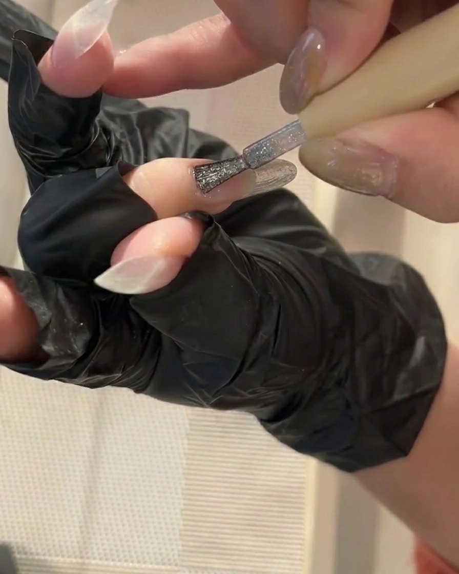 Un petit pinceau appliquant une fine couche de base gel transparente sur un ongle propre.