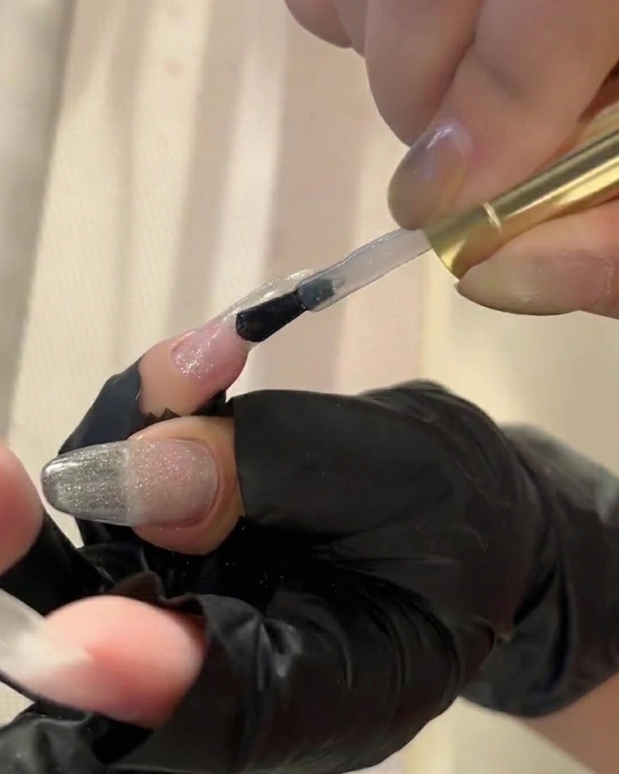 Un pinceau appliquant un top coat transparent sur un ongle, le préparant pour lapplication de la poudre pigmentée.