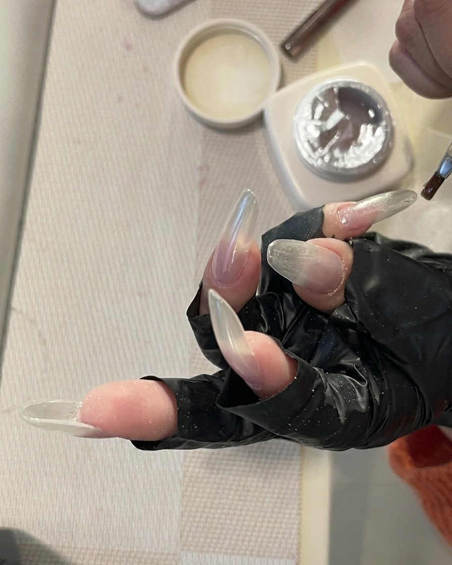 Une main avec de longs ongles transparents reposant à lintérieur dune lampe à ongles UV/LED professionnelle, les ongles étant éclairés par la lumière.