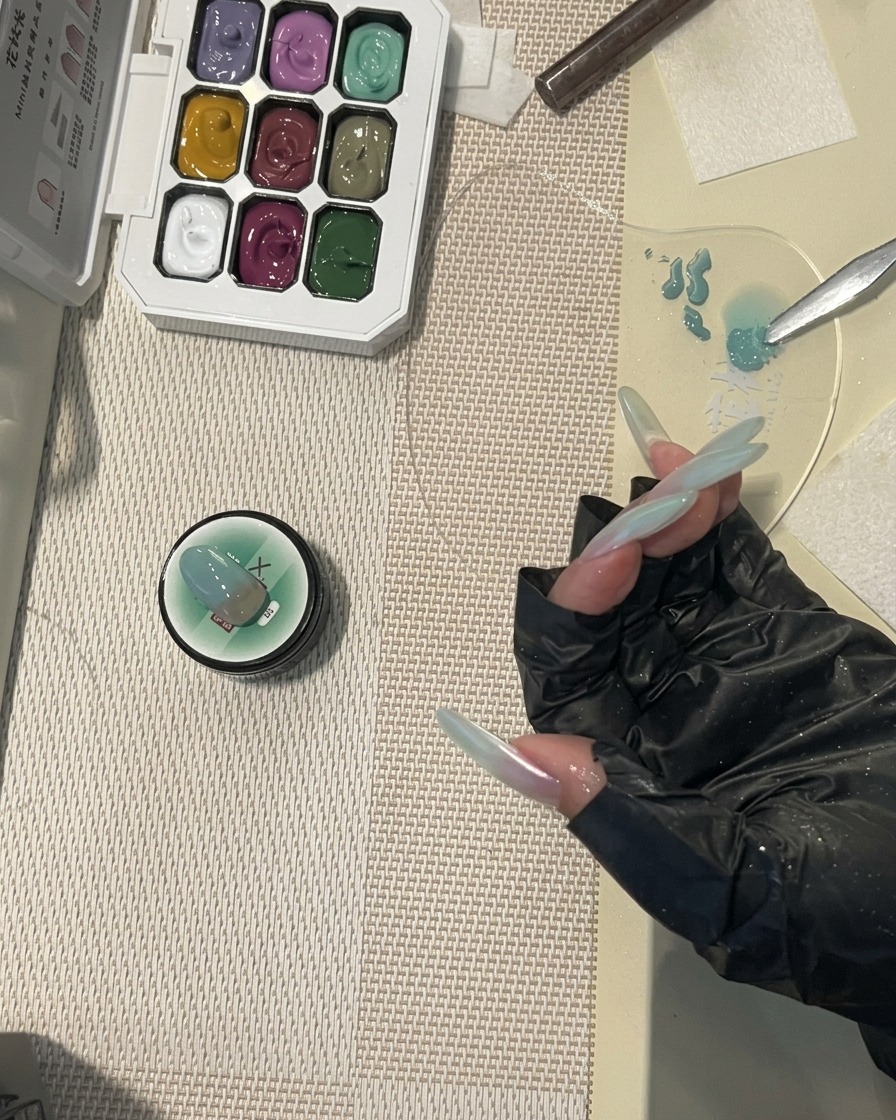 Un pinceau à ongles appliquant un top coat final brillant sur un long ongle présentant un motif dégradé vert menthe.