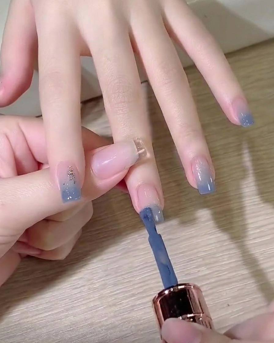 Un pinceau de vernis en gel appliquant une couleur bleu poudré sur le bout dun ongle préparé.