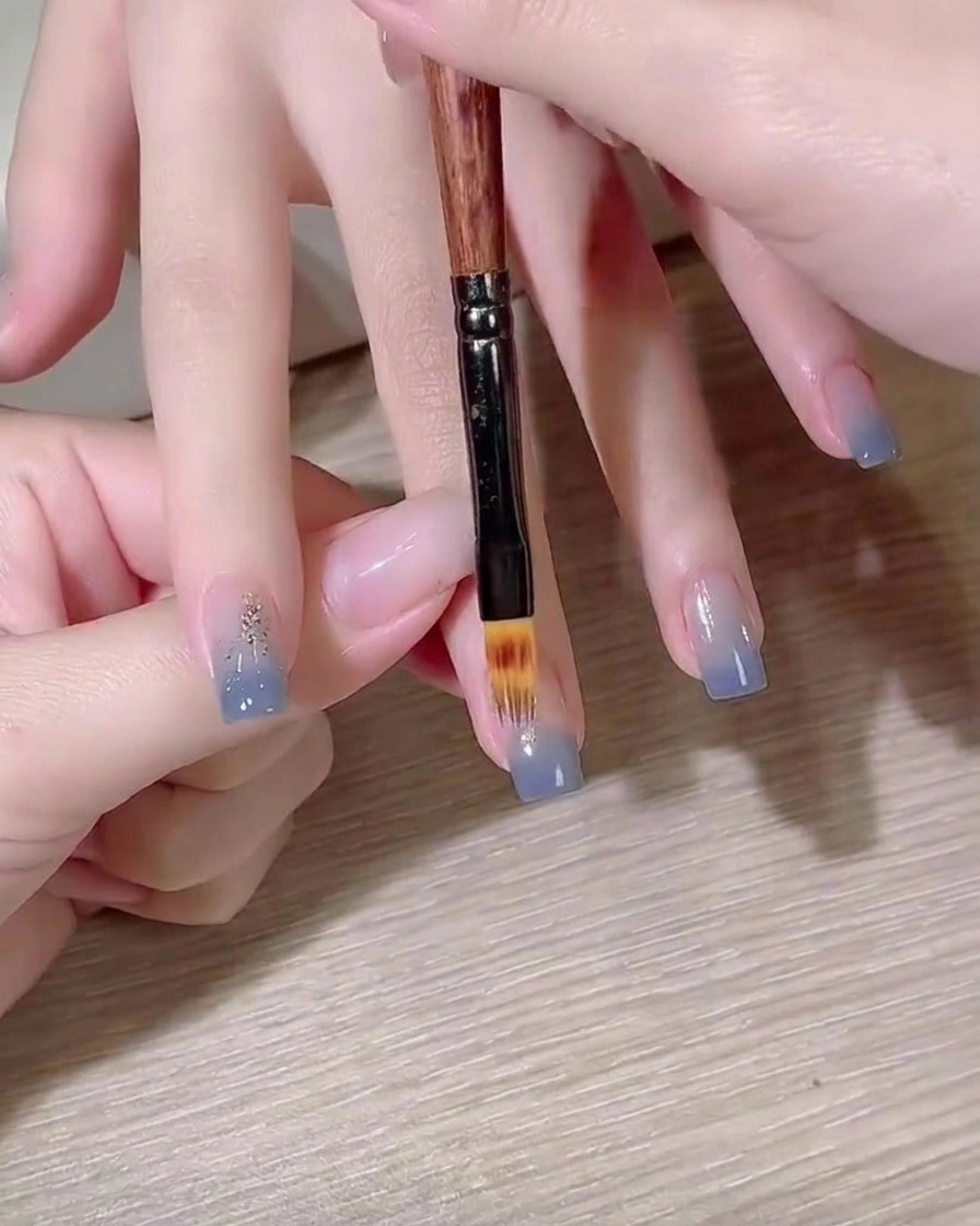 Un pinceau plat pour gel estompant un dégradé de couleur bleue sur un ongle.