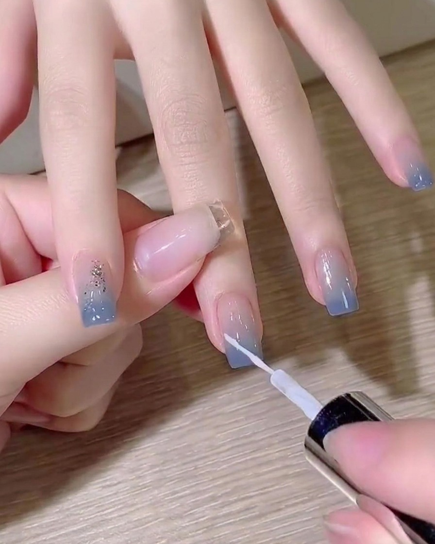 Un pinceau liner fin traçant une fine ligne diagonale blanche sur un ongle dégradé.
