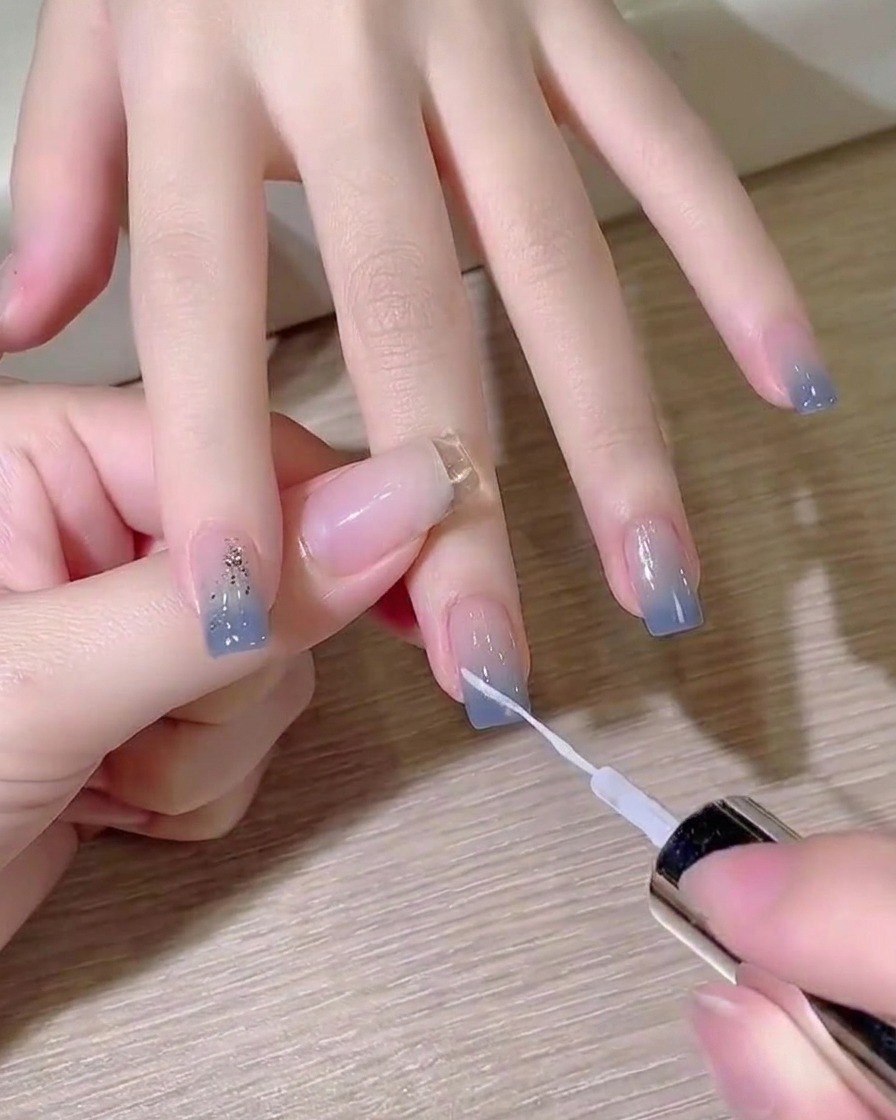 Un pinceau liner fin peignant une ligne blanche diagonale très nette sur un ongle ombré bleu.