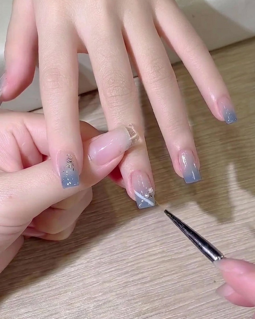 Un pinceau de détail appliquant une petite goutte de gel de construction transparent sur la surface de longle en guise de colle.