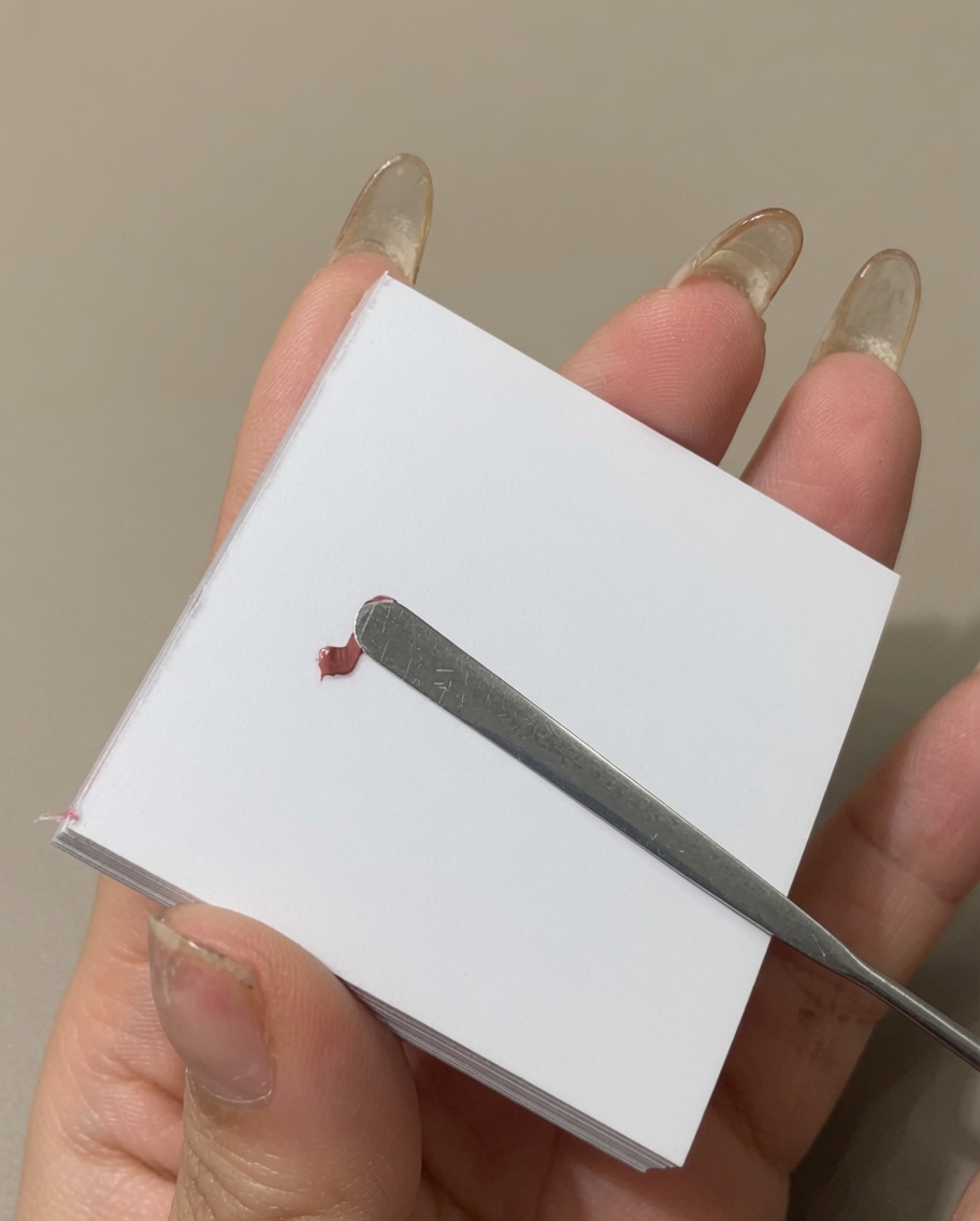 Une spatule métallique étalant une ligne de vernis gel coloré sur la surface dune palette.