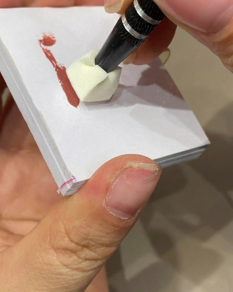 Une éponge de maquillage tamponnant du gel coloré sur la pointe dun ongle à base nude pour créer un effet ombré.