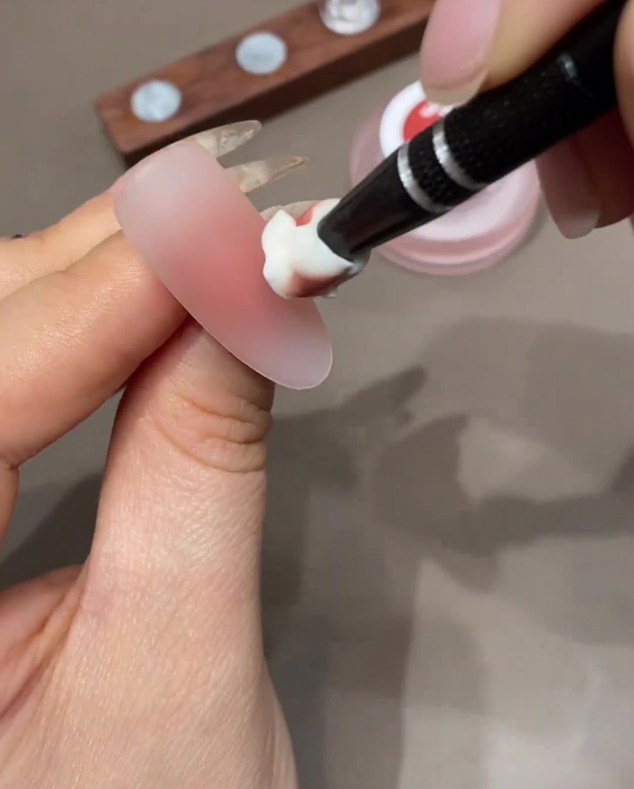 Une éponge de maquillage appliquant une couche de gel coloré sur la pointe dun ongle pour construire un dégradé ombré.