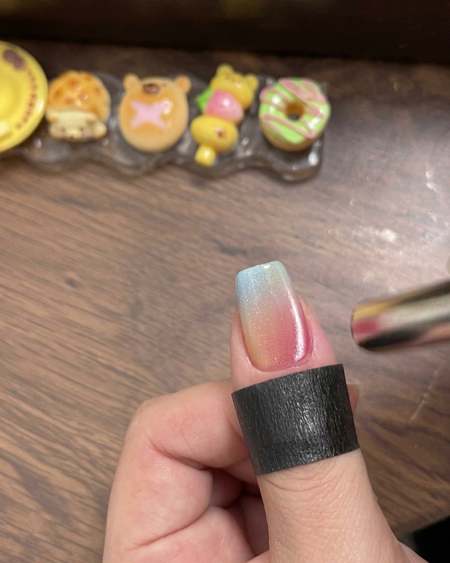 Un pinceau appliquant un top coat brillant transparent sur longle dégradé multicolore.
