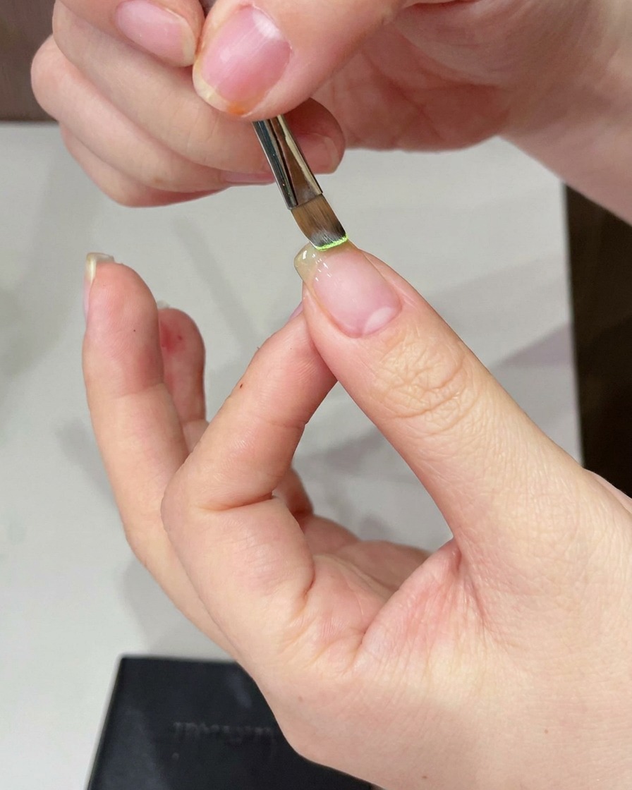 Un pinceau de précision applique du gel vert clair sur le bout de longle nu.