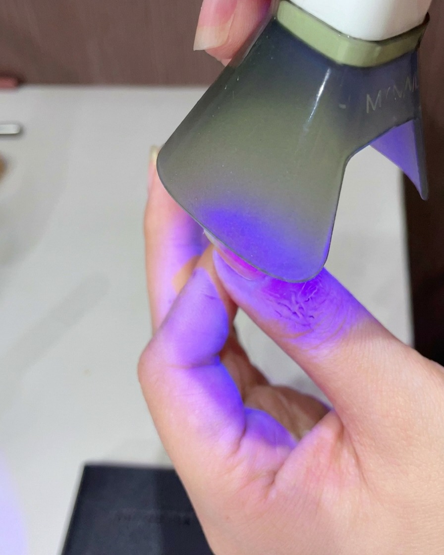 Gros plan sur un doigt sous une petite lampe UV/LED pour catalyser le top coat brillant.