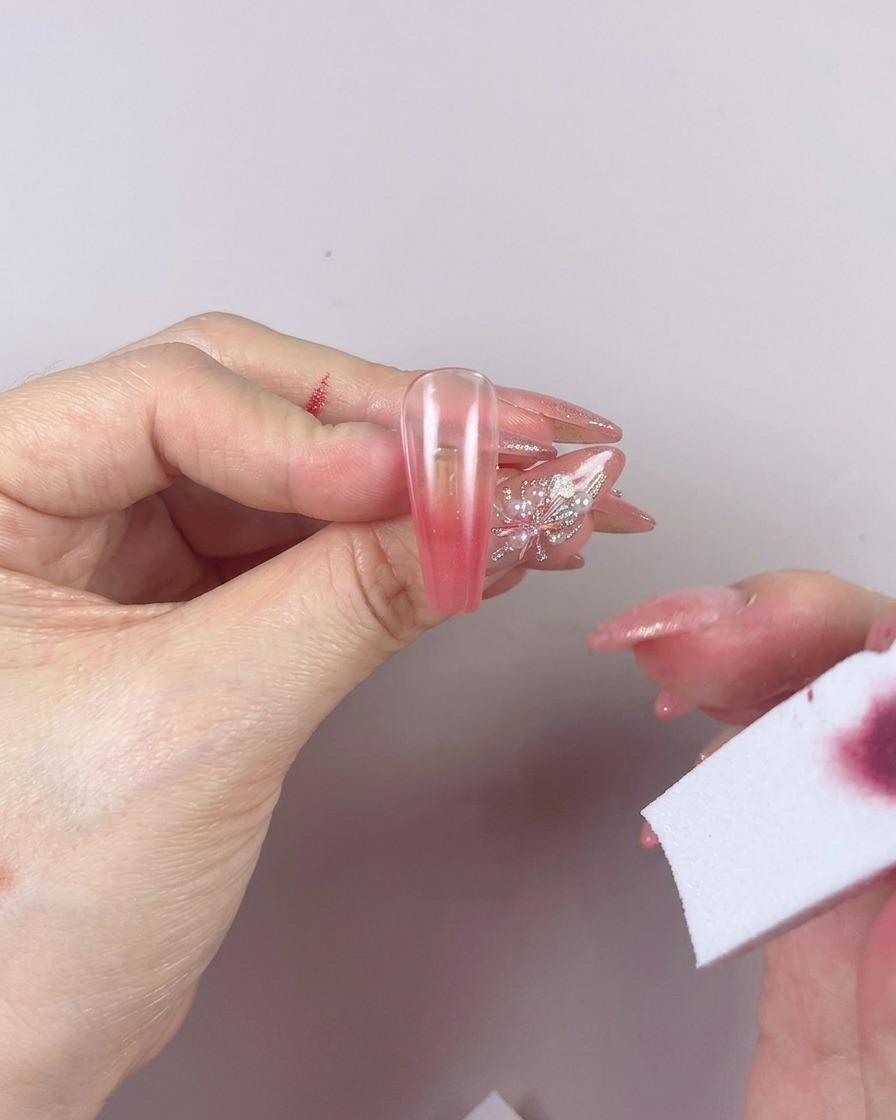 Une éponge utilisée pour estomper la couleur du gel sur un ongle avec des mouvements horizontaux de gauche à droite.