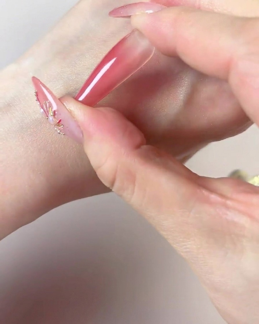 Une main utilisant le centre foncé dune éponge à maquillage pour ajouter de la couleur concentrée à la pointe dun ongle long.