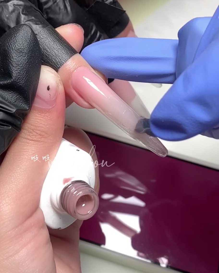 Gros plan dun pinceau appliquant un gel magenta vif sur la moitié extérieure de longle.