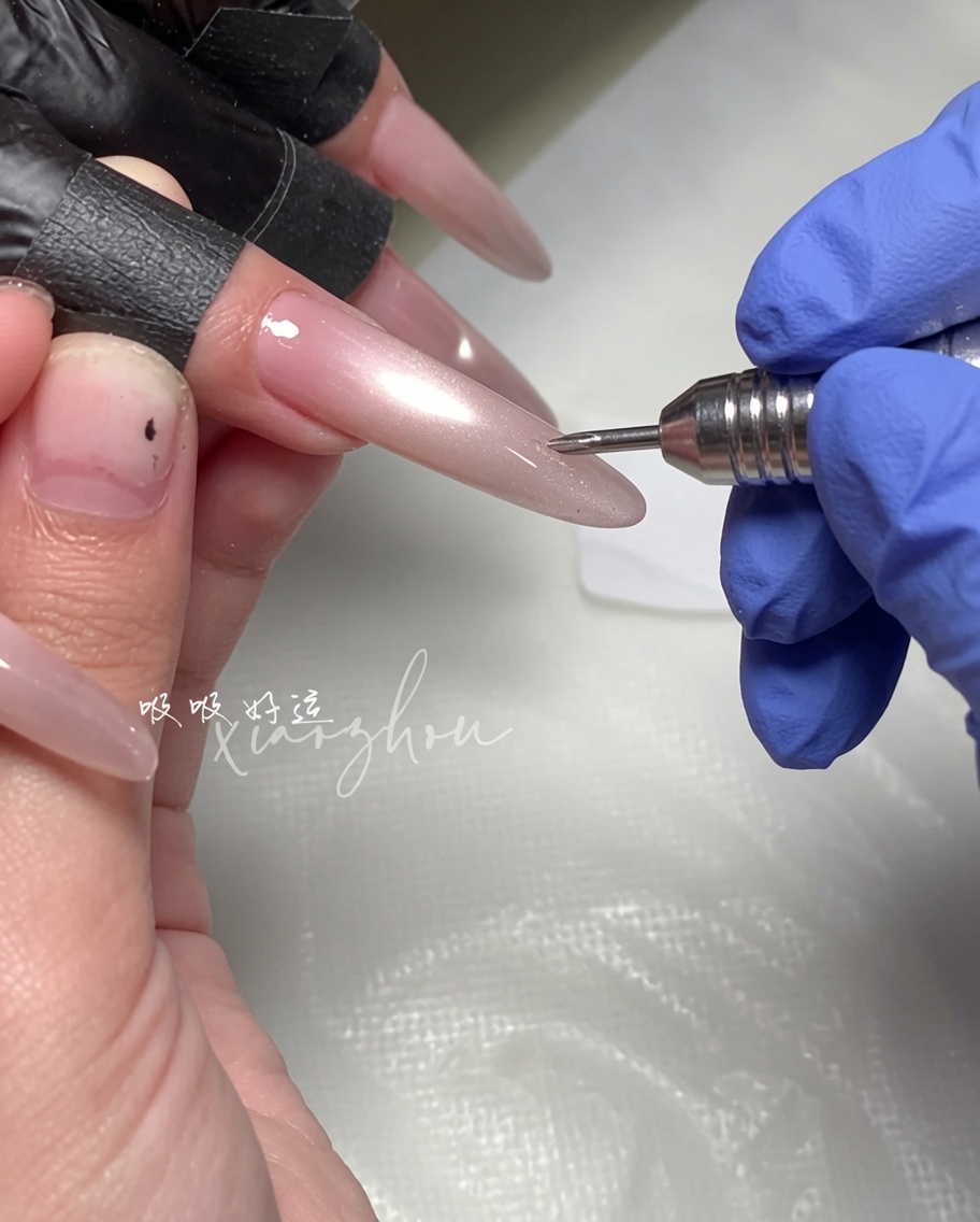 Une main tenant un aimant au-dessus dun ongle long en amande recouvert de vernis magnétique magenta humide.
