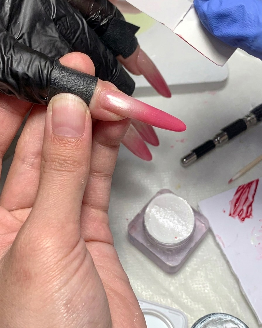Gros plan dune lingette non pelucheuse nettoyant la peau et les bords autour dun ongle au dégradé magenta.