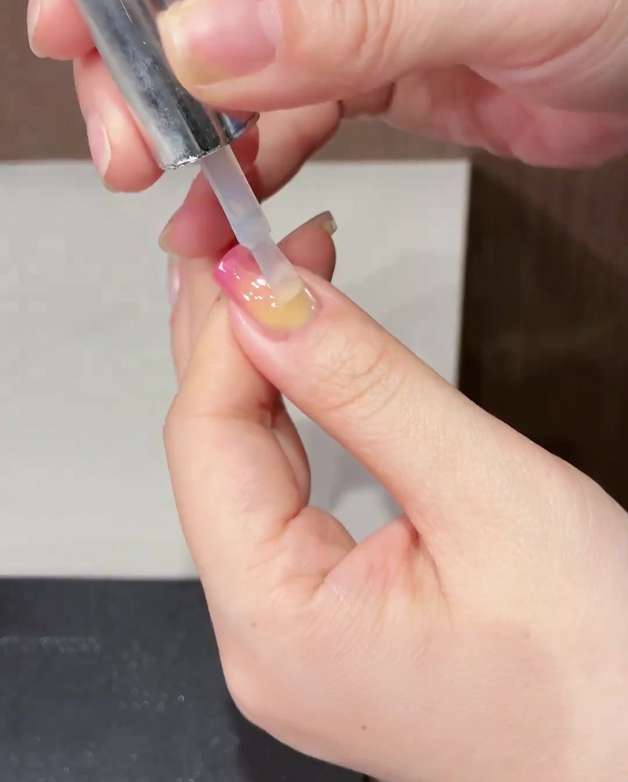 Un pinceau appliquant un top coat transparent brillant sur le design terminé.