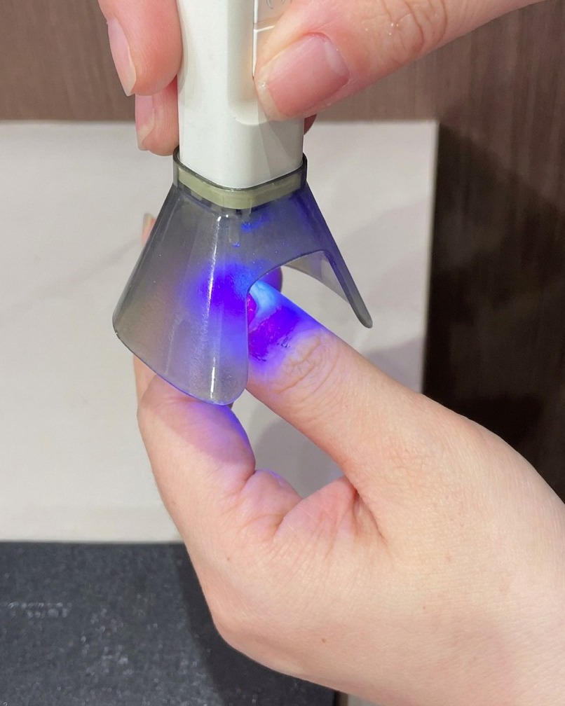 Un doigt placé sous une lampe UV pour létape finale de durcissement.