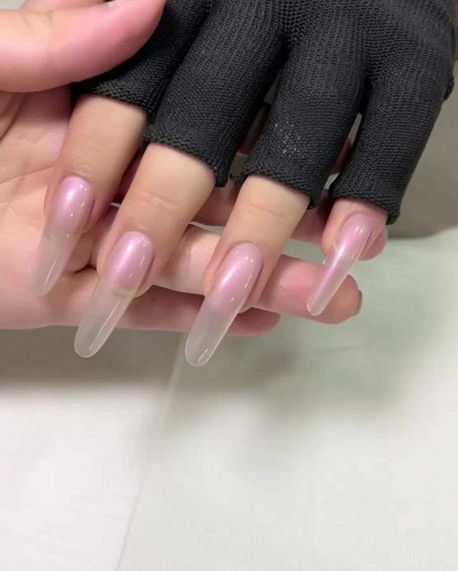 Gros plan sur une main aux ongles longs en forme damande dont les cuticules sont repoussées à laide dun repousse-cuticules métallique.