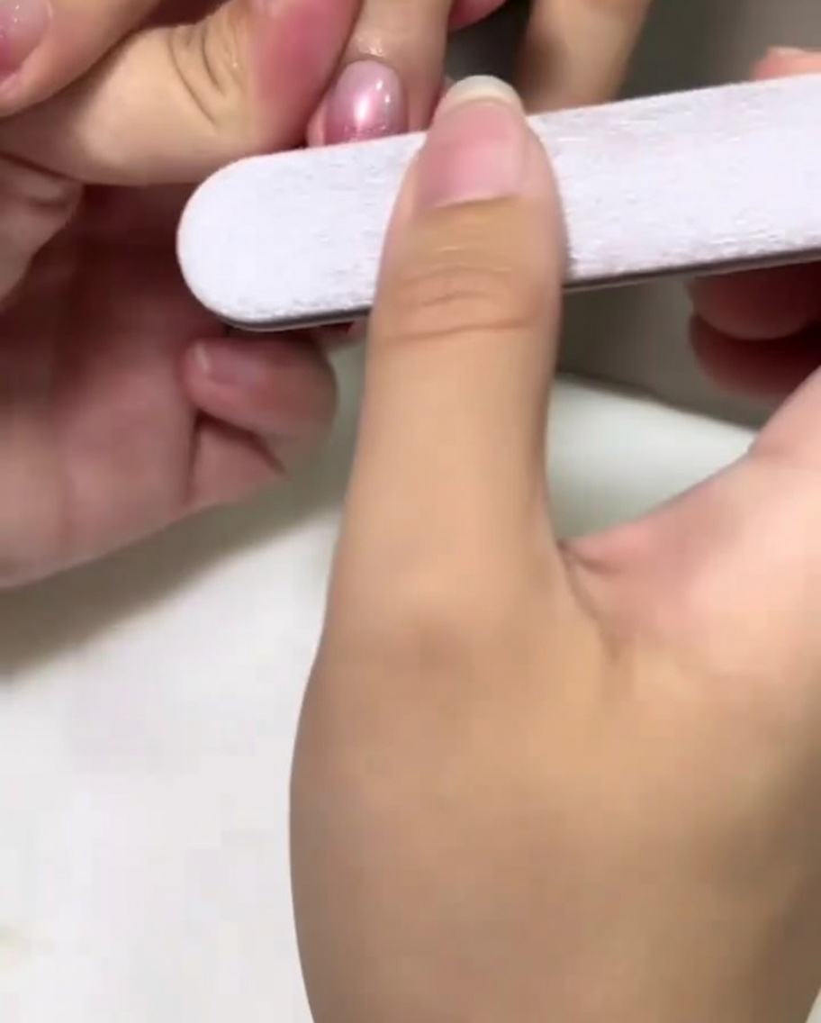Une main tenant une lime à ongles polissant doucement le centre dun ongle verni en rose.