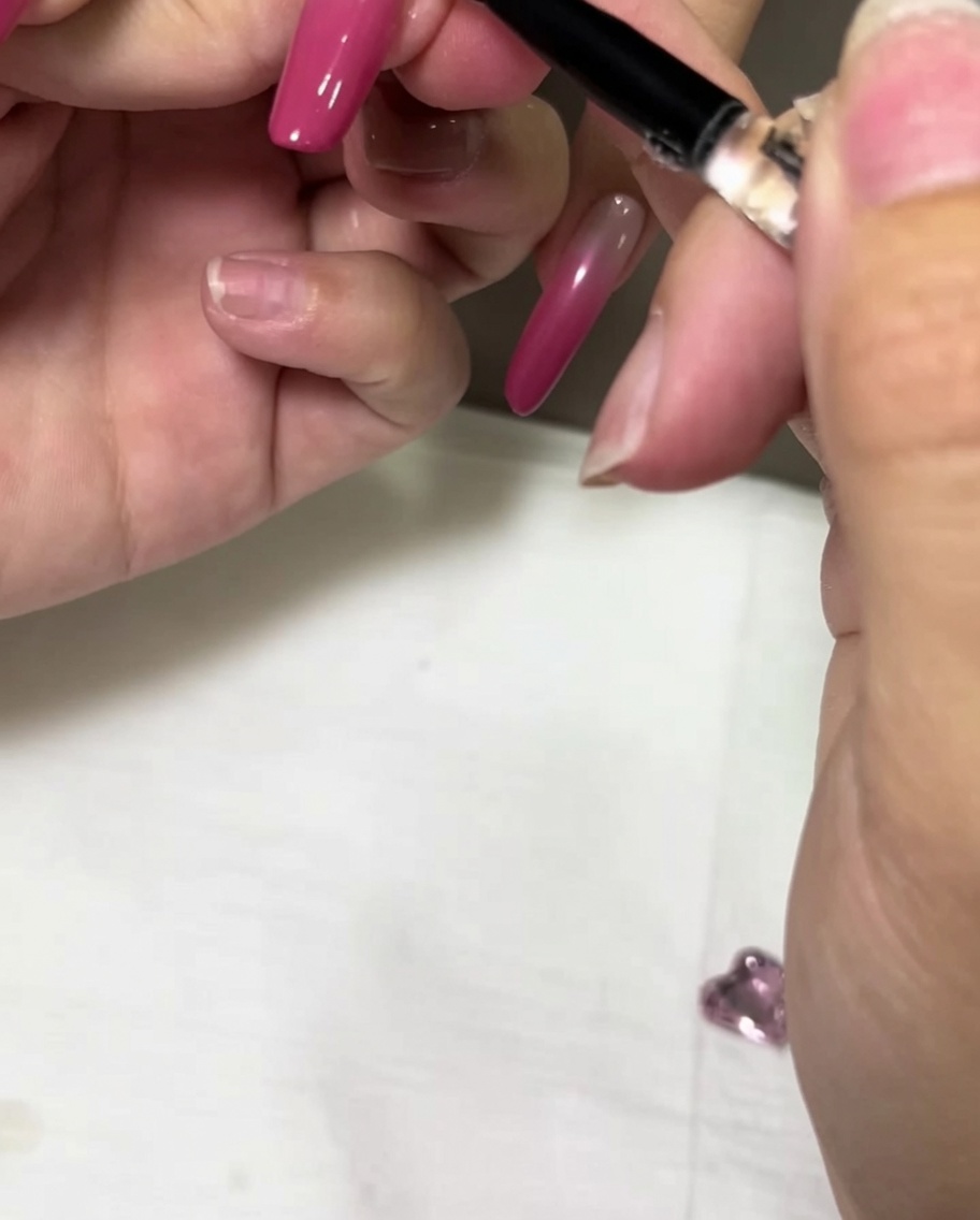 Un pinceau de précision appliquant une perle dadhésif gel transparent sur un ongle en dégradé rose.