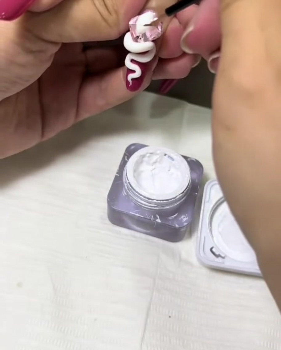 Un pinceau fin appliquant du gel blanc pour texturer le design 3D sur longle.