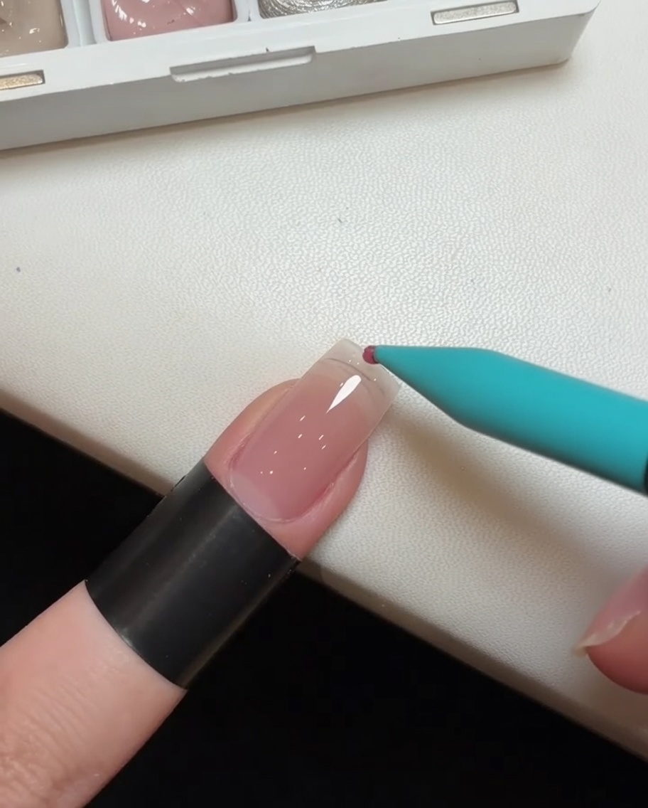 Gros plan dun pinceau de détail appliquant une goutte de vernis gel rose sur la pointe dune extension dongle transparentecite: 1.