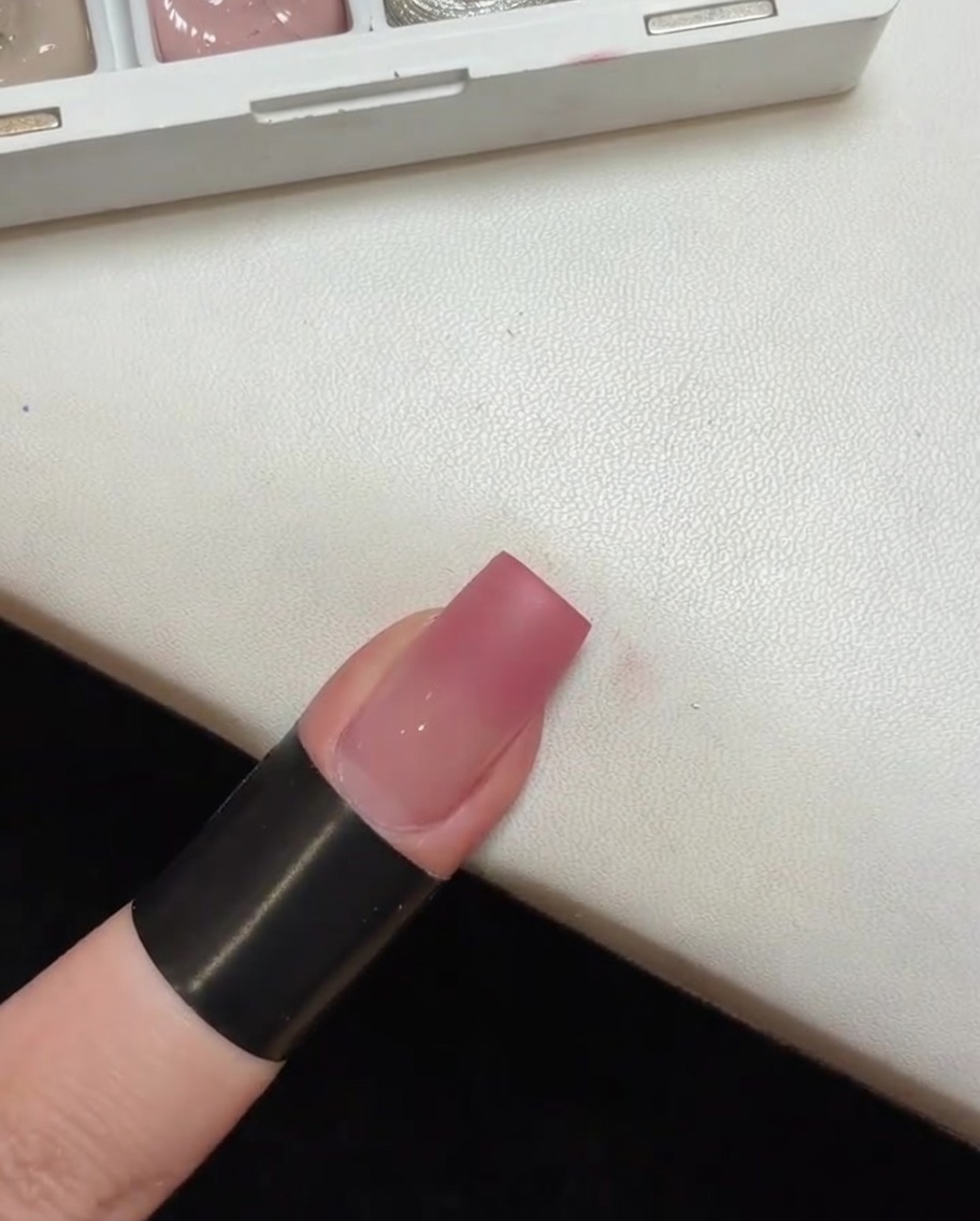 Un ongle avec une base dégradée rose en train de catalyser sous une petite lampe UV portablecite: 1.