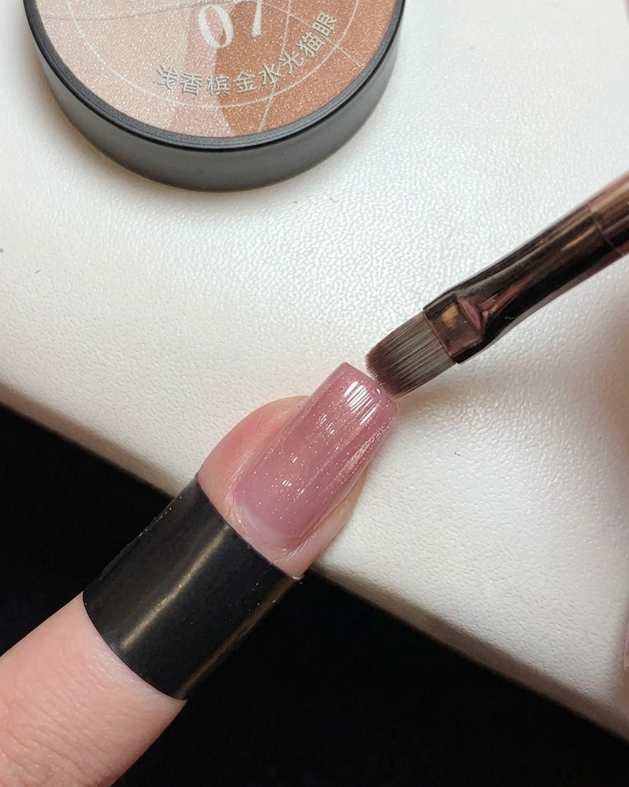 Un pinceau appliquant un gel magnétique rose translucide avec des reflets dorés sur un ongle préalablement catalysé avec un dégradé rosecite: 1.