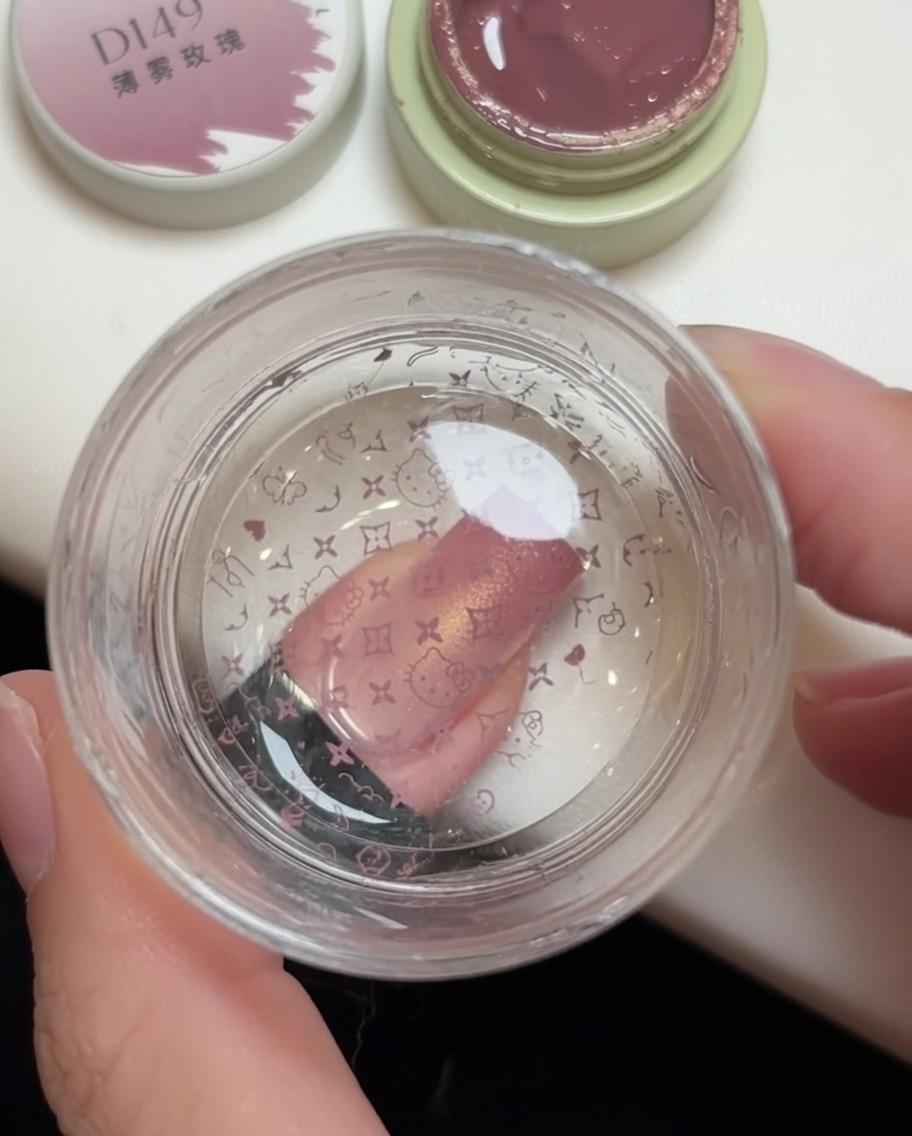 Un tampon en silicone pressant un motif rose sur un ongle, avec le dessin de Hello Kitty visible sur la tête du tamponcite: 1.
