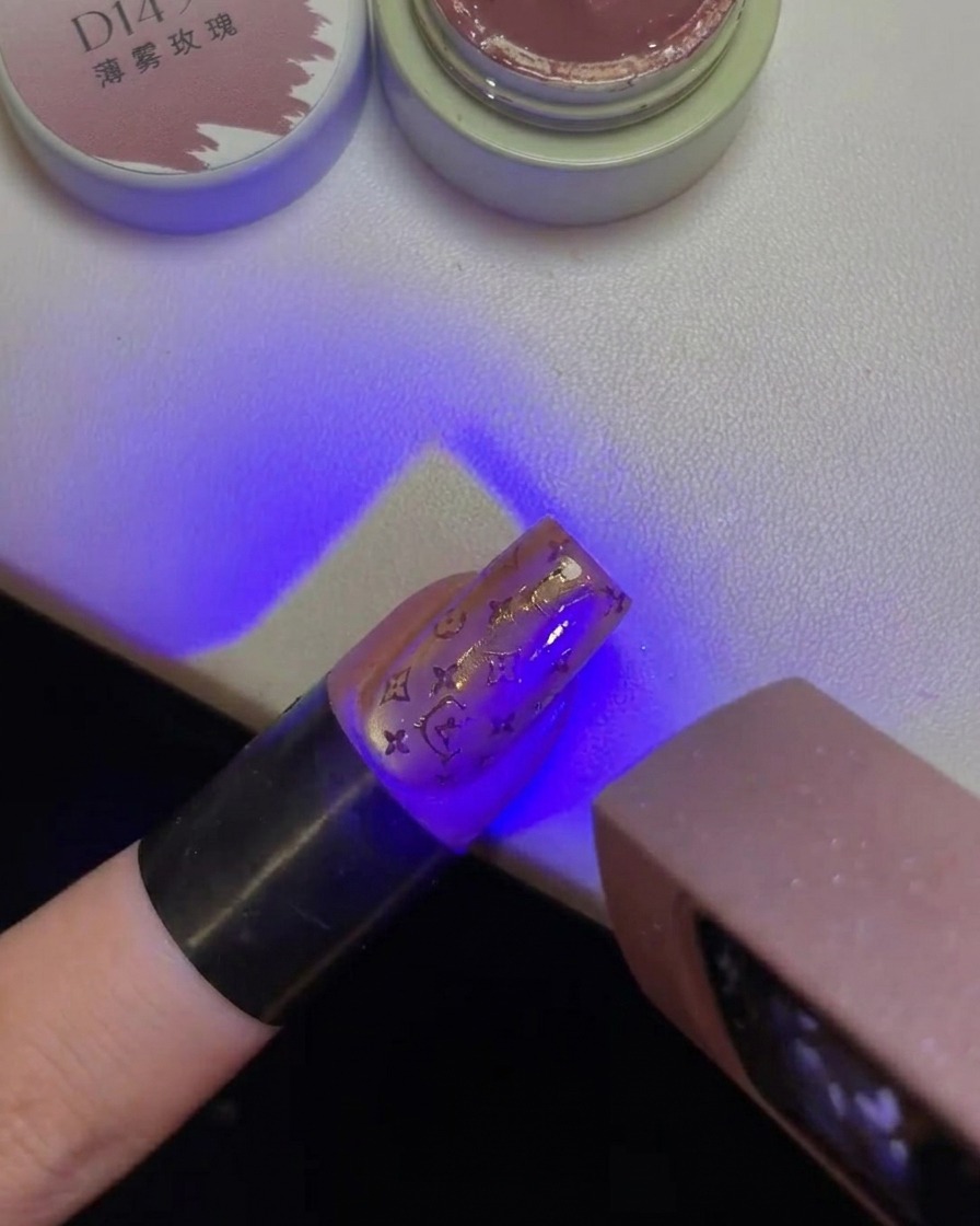 Un doigt avec un motif Hello Kitty estampé sur longle maintenu sous la lumière violette dune lampe UVcite: 1.