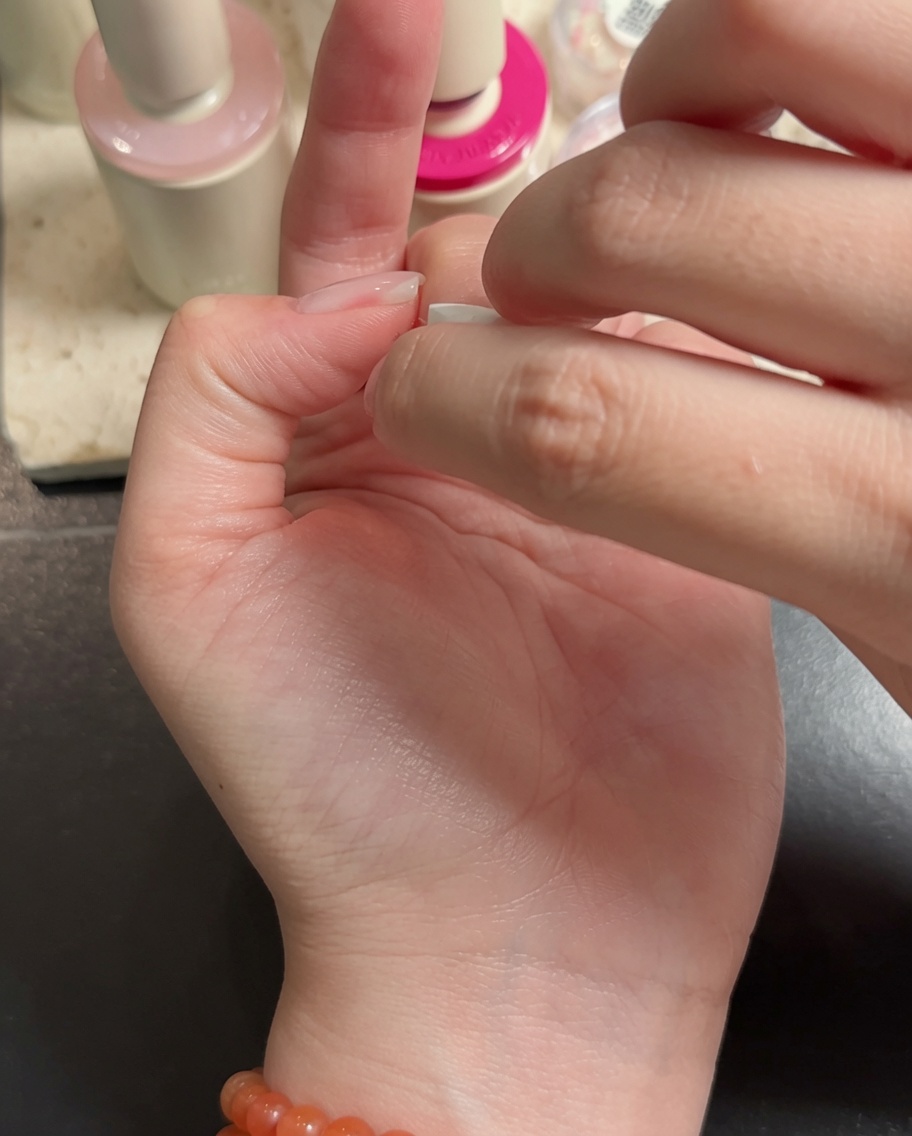 Un pinceau nail art appliquant du gel blanc sur les pointes des doigts, créant un effet dégradé.